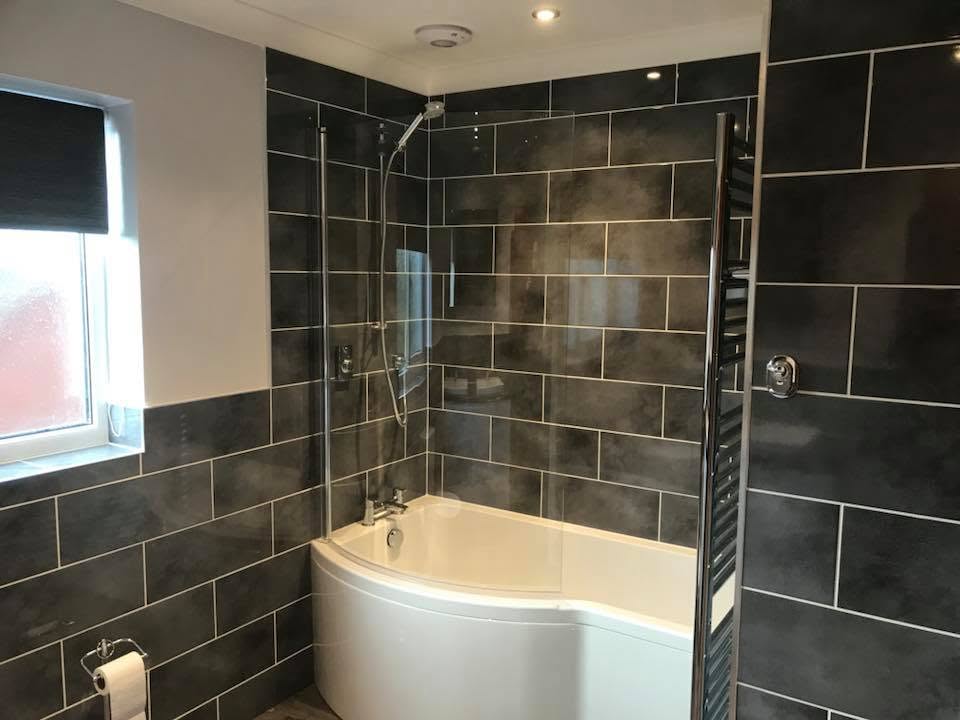 New bathroom with dark wall tiles, walk-in shower over a curved bath